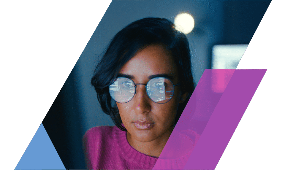 A woman wearing glasses focuses intently on a computer screen, visible code reflected in her lenses.